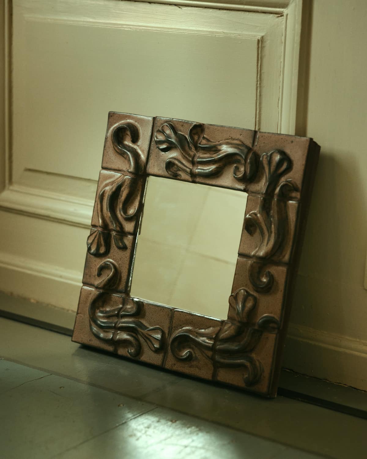 Mirror framed in relief tiles, leaning against a panelled wall